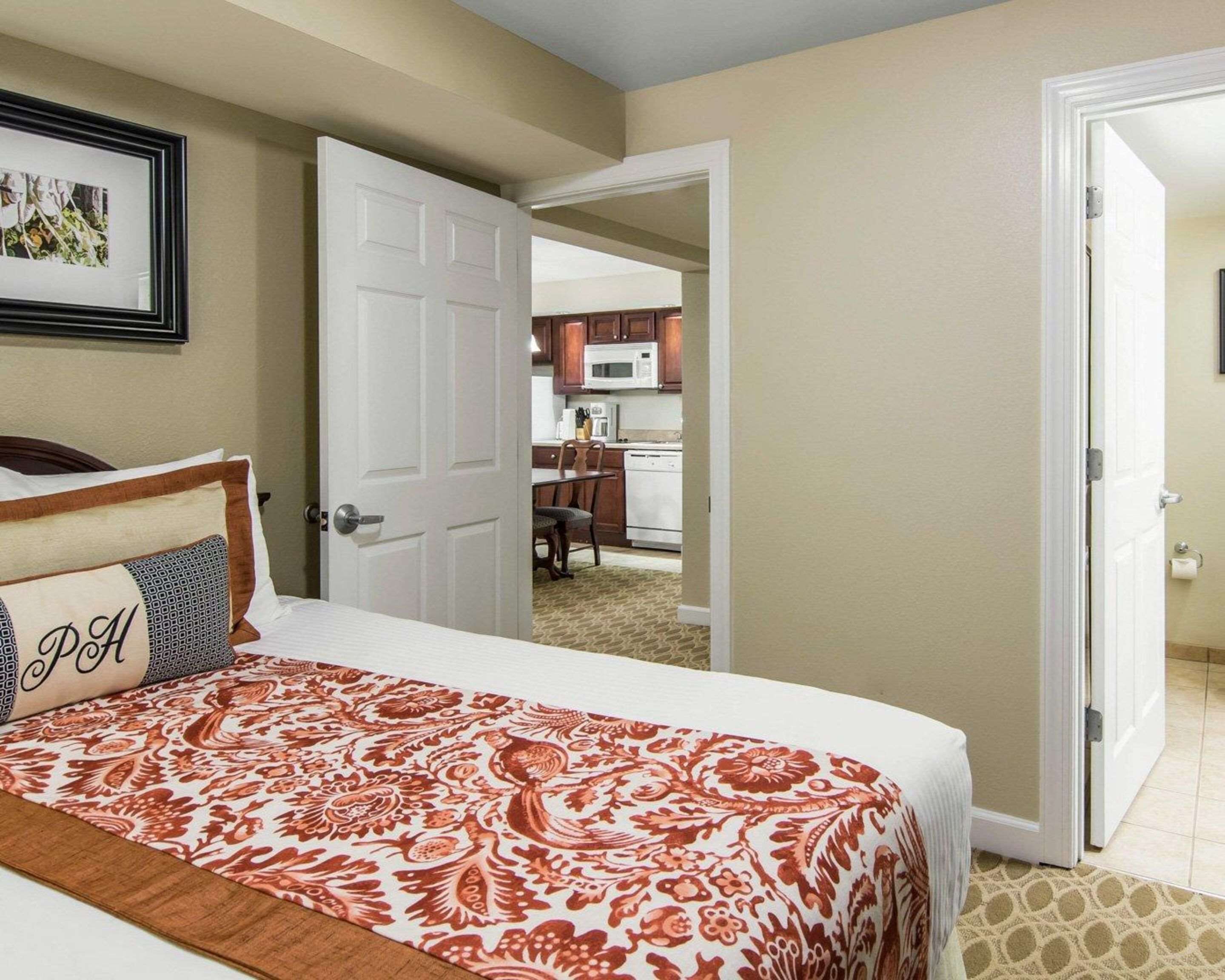 A hotel room with a bed, a door leading to a kitchen, and a framed picture on the wall.