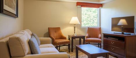 Habitación de hotel con sofá, dos sillones, una mesa de centro, televisor y lámpara.