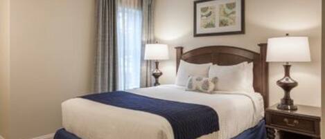 A hotel room with a large bed, two bedside lamps, a ceiling fan, and a framed picture on the wall.