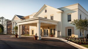 A two-story hotel with a covered entrance, large windows, and a brick facade. - Bluegreen Vacations Patrick Henry Square, an Ascend Collection Resort (Williamsburg)