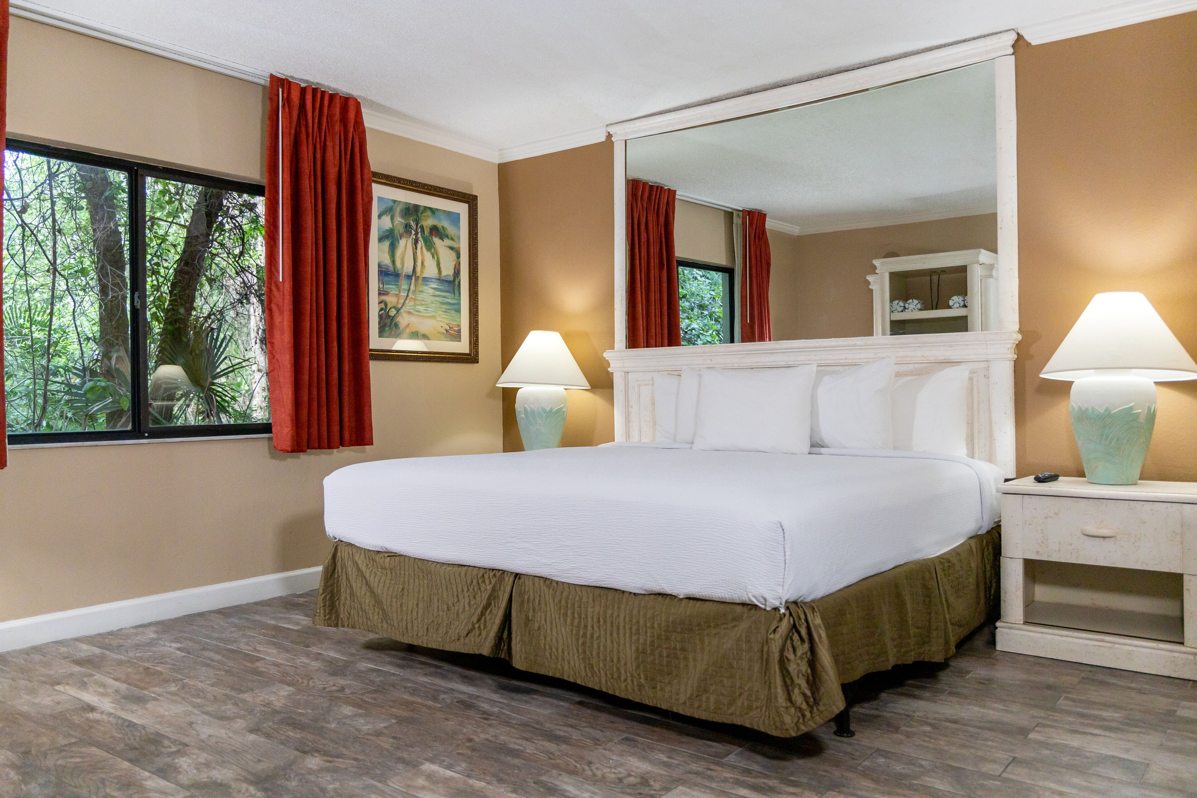 A hotel room with a large bed, a nightstand, a mirror, and a window with curtains.