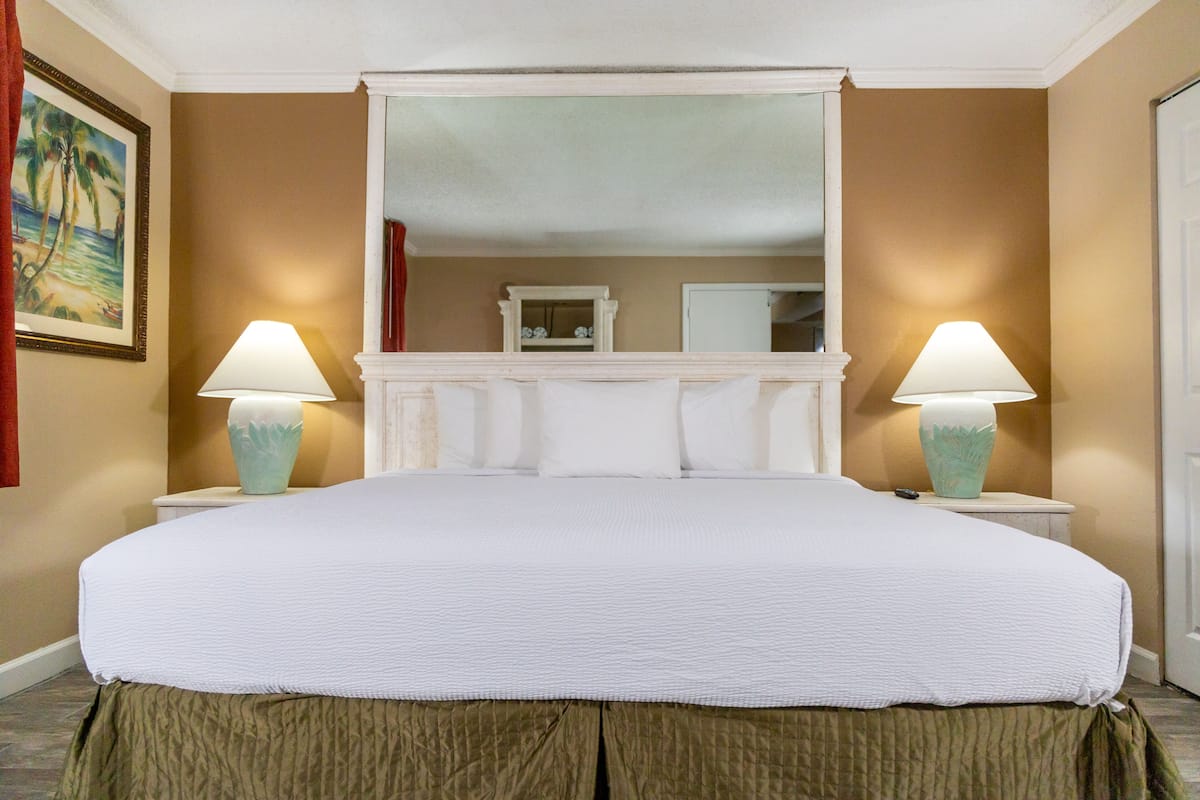 A hotel room with a large bed, two bedside lamps, a mirror above the bed, and a painting on the wall.
