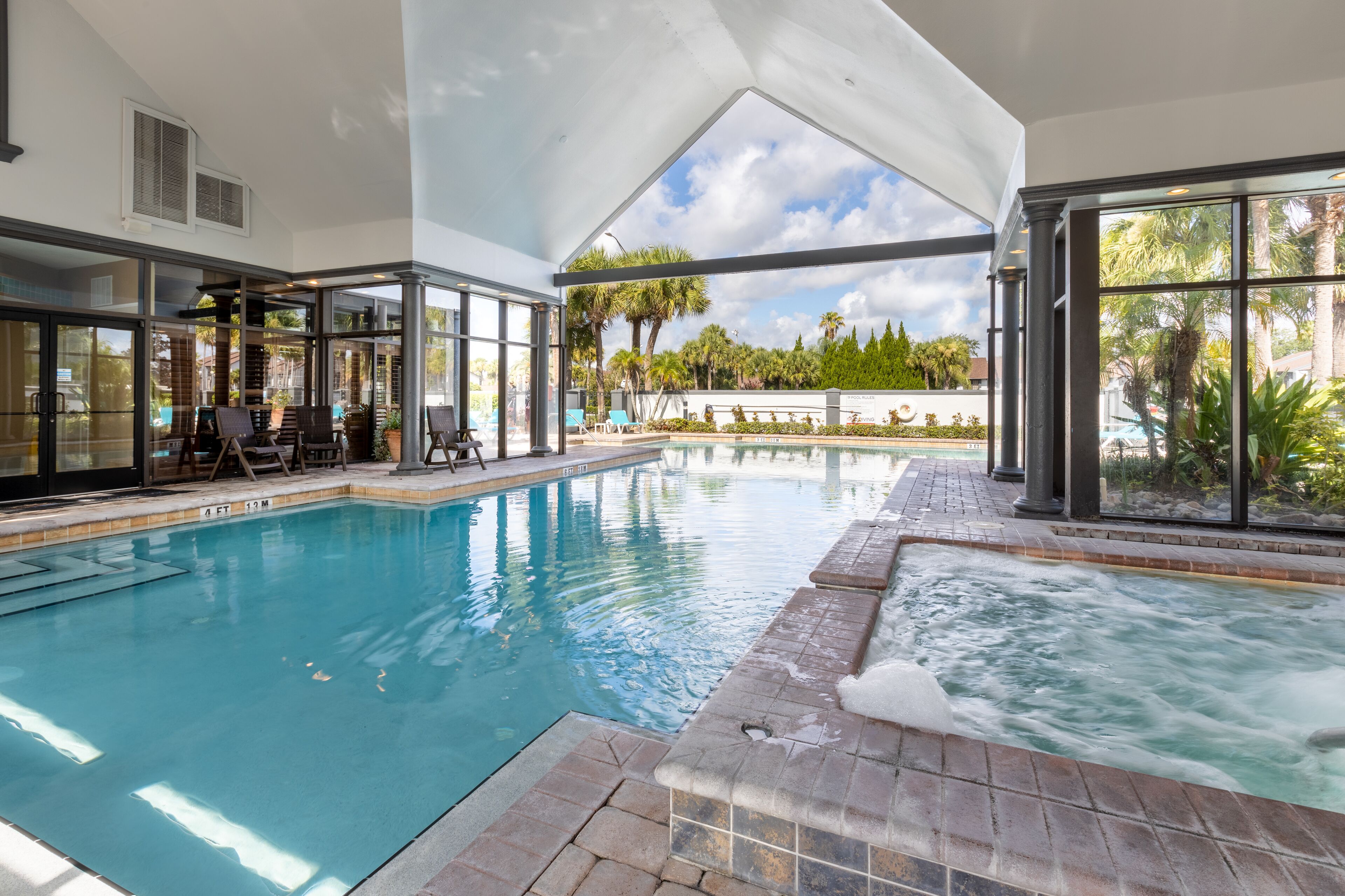 Una piscina interior con paredes de vidrio transparente, un jacuzzi y una zona de patio con sillones de relax.