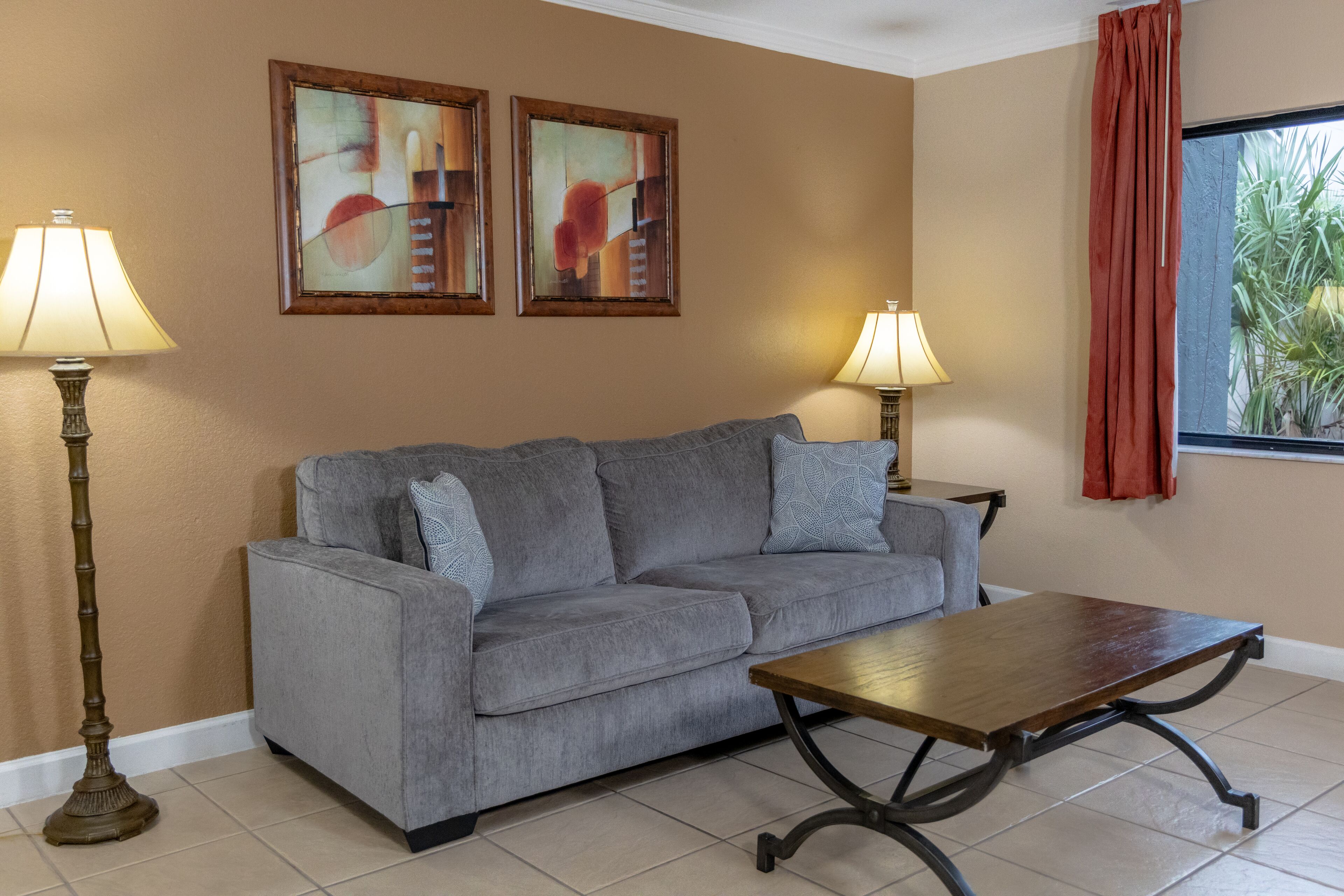 A living room with a gray sofa, two lamps, and two abstract paintings on the wall.
