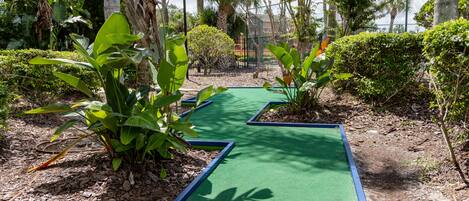 Un parcours de mini-golf doté d’un gazon synthétique vert, entouré de diverses plantes et arbres tropicaux.