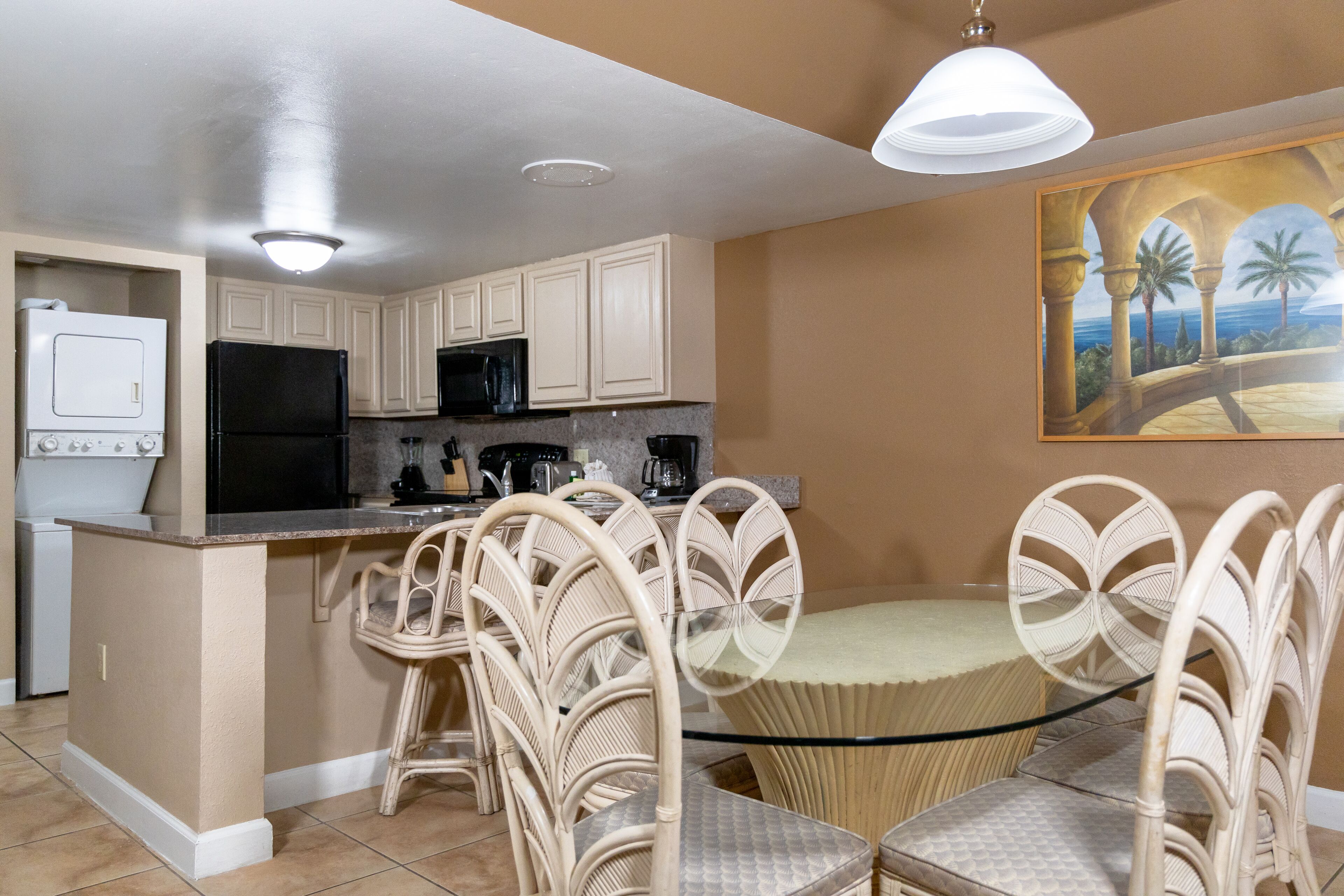 A kitchen with white cabinets, a black refrigerator, and a dining area with wicker chairs and a glass table.