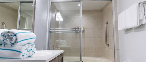 A bathroom with a glass-enclosed shower, a white toilet, and a sink with a towel on the counter.