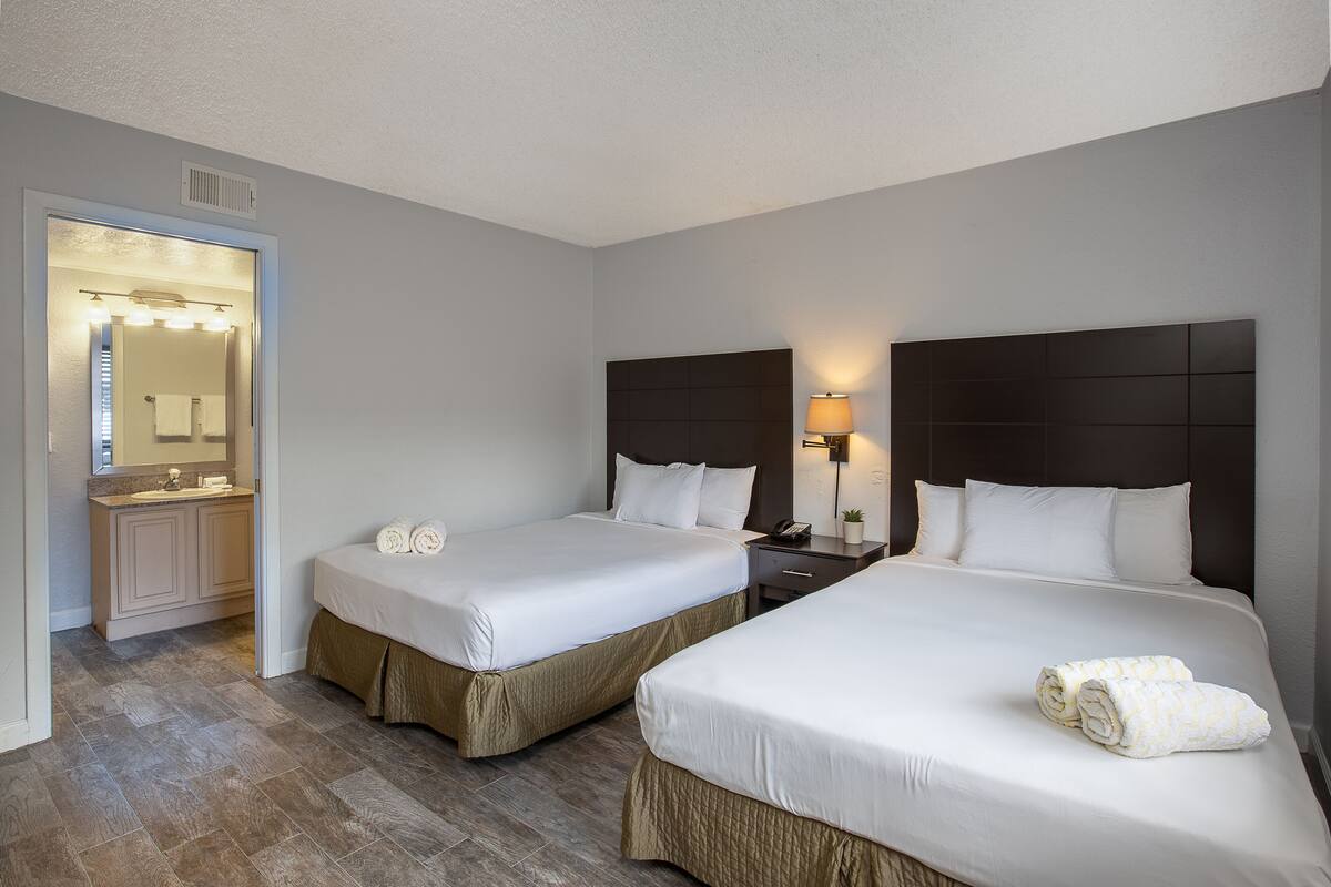 A hotel room with two beds, a bathroom with a vanity, and a mirror.