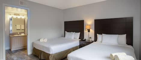 Habitación de hotel con dos camas, un baño con tocador y espejo.