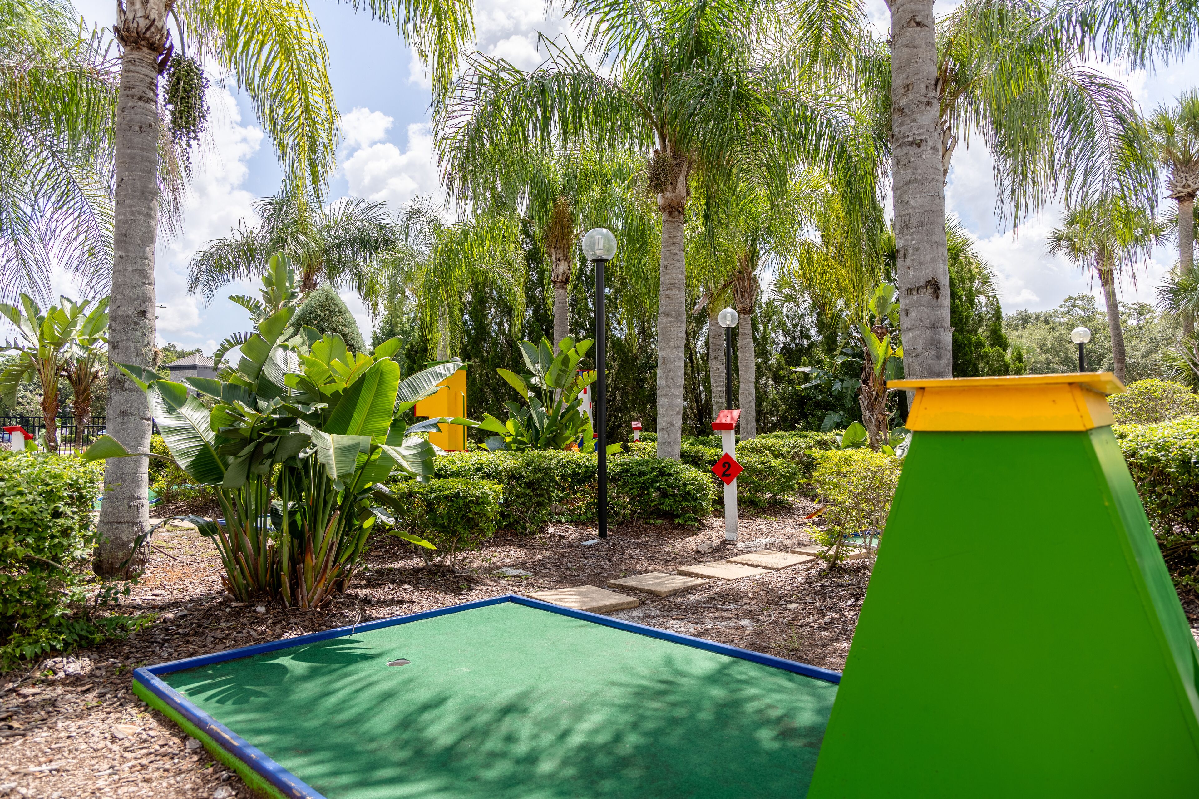 A miniature golf course with a green putting green, palm trees, and a yellow and green structure.
