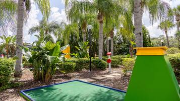 Un campo de mini golf con un putting verde, palmeras y una estructura verde y amarilla.