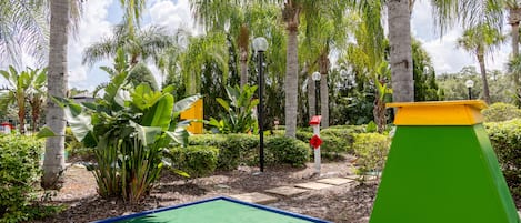 Un campo de mini golf con un putting verde, palmeras y una estructura verde y amarilla.