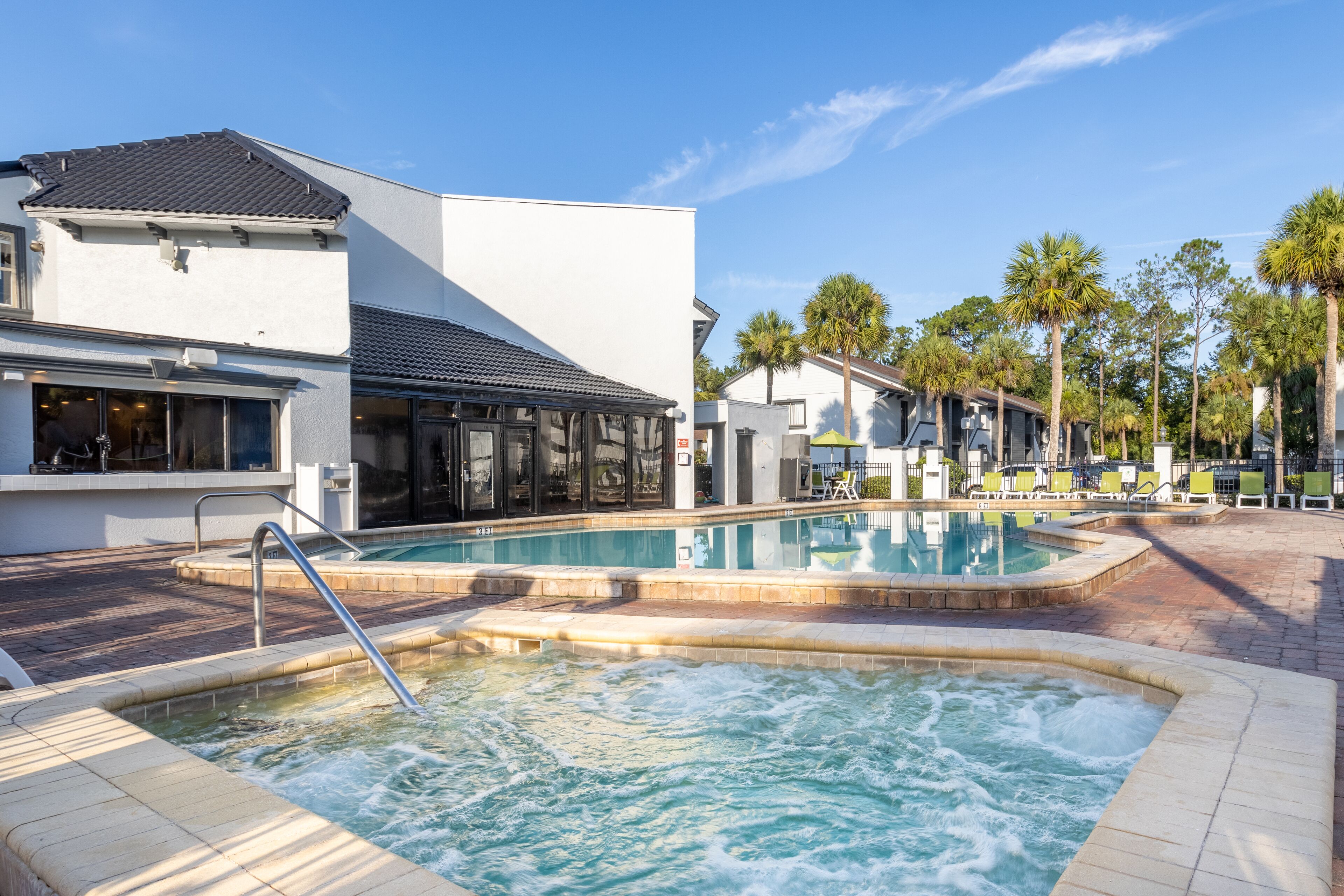 A pool area with a hot tub, lounge chairs, and a building with large windows and a covered patio.