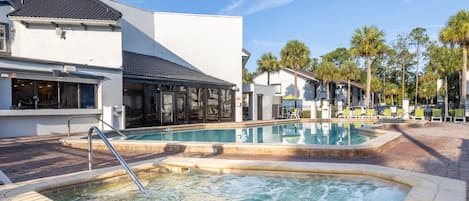 A pool area with a hot tub, lounge chairs, and a building with large windows and a covered patio.