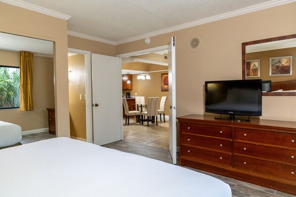 A hotel room with a bed, a TV on a wooden dresser, a dining area with chairs and a table, and a kitchen in the background. - Legacy Vacation Resorts - Kissimmee/Orlando (Kissimmee)
