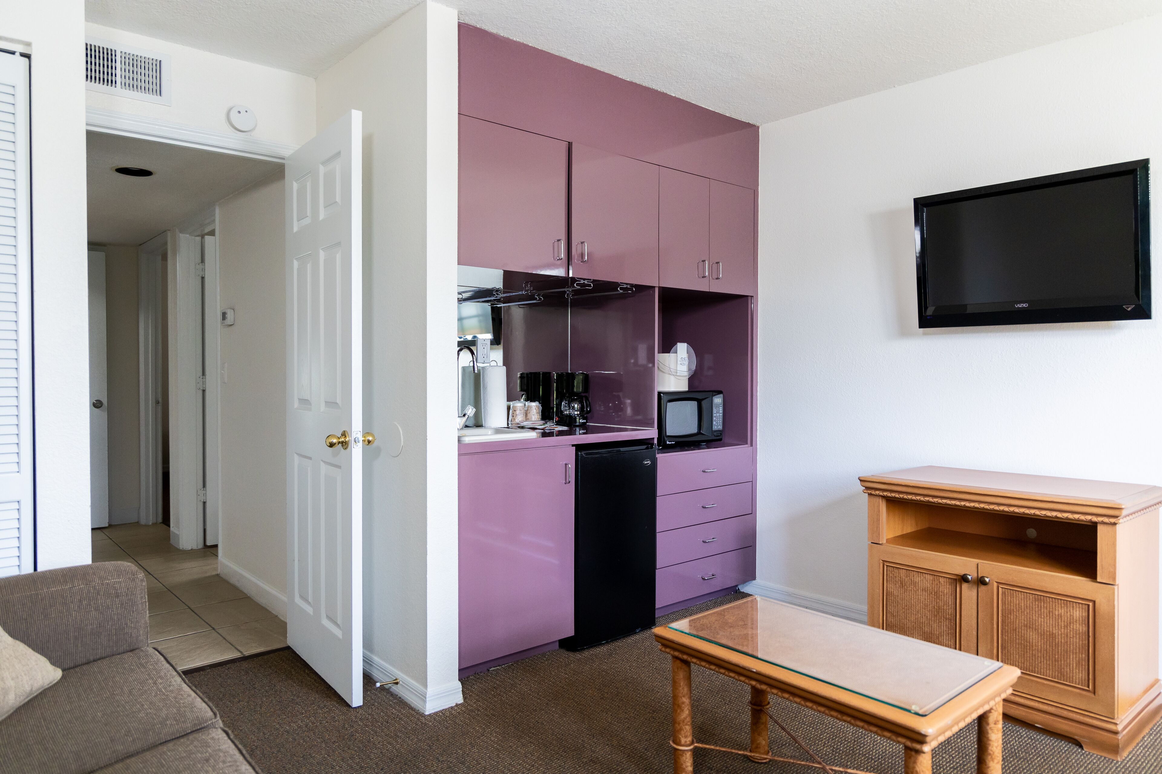 Une cuisine de taille réduite avec des meubles de couleur violette, un réfrigérateur noir, un four à micro-ondes et un meuble en bois.