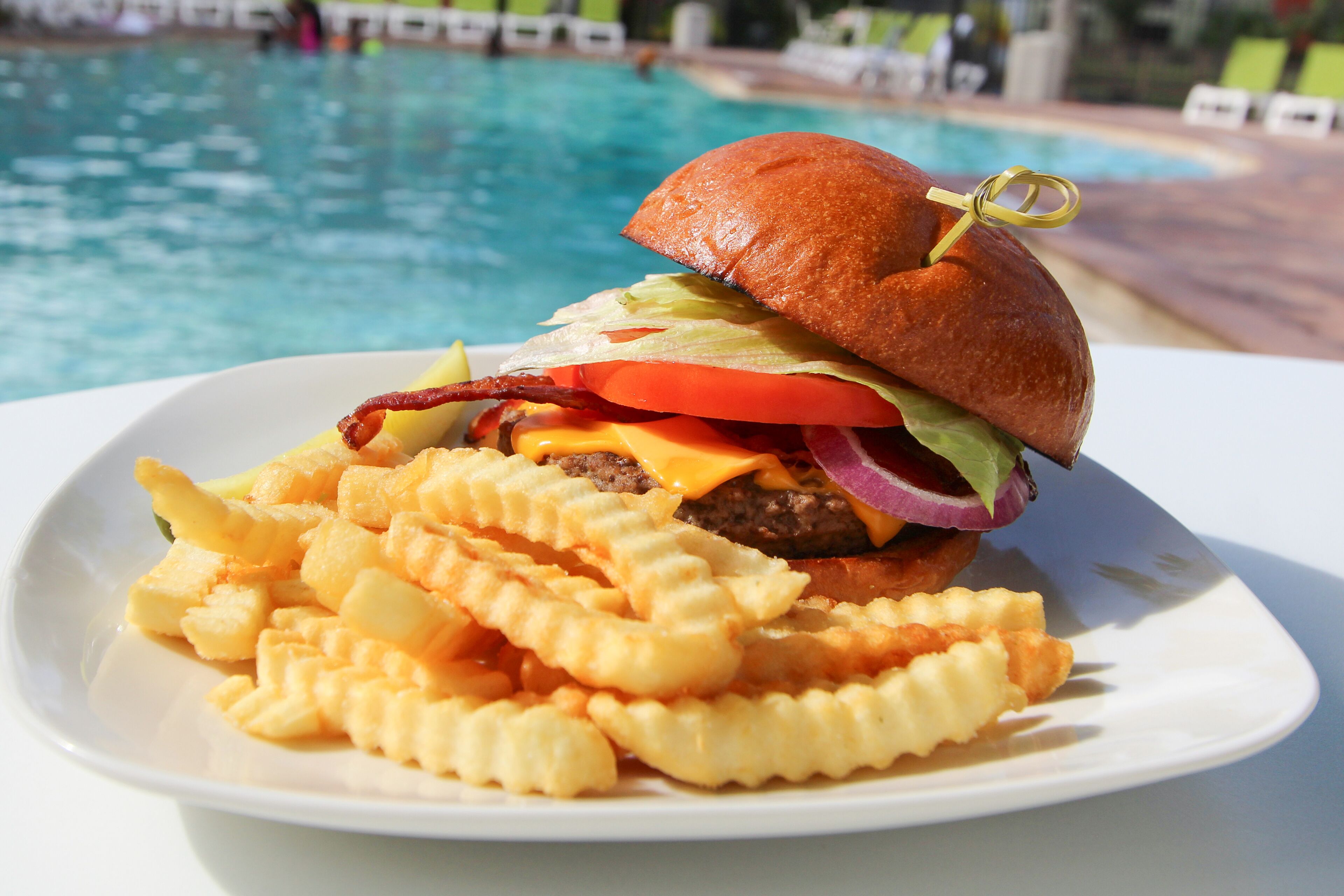 Um prato com hambúrguer e batatas fritas perto de uma piscina.
