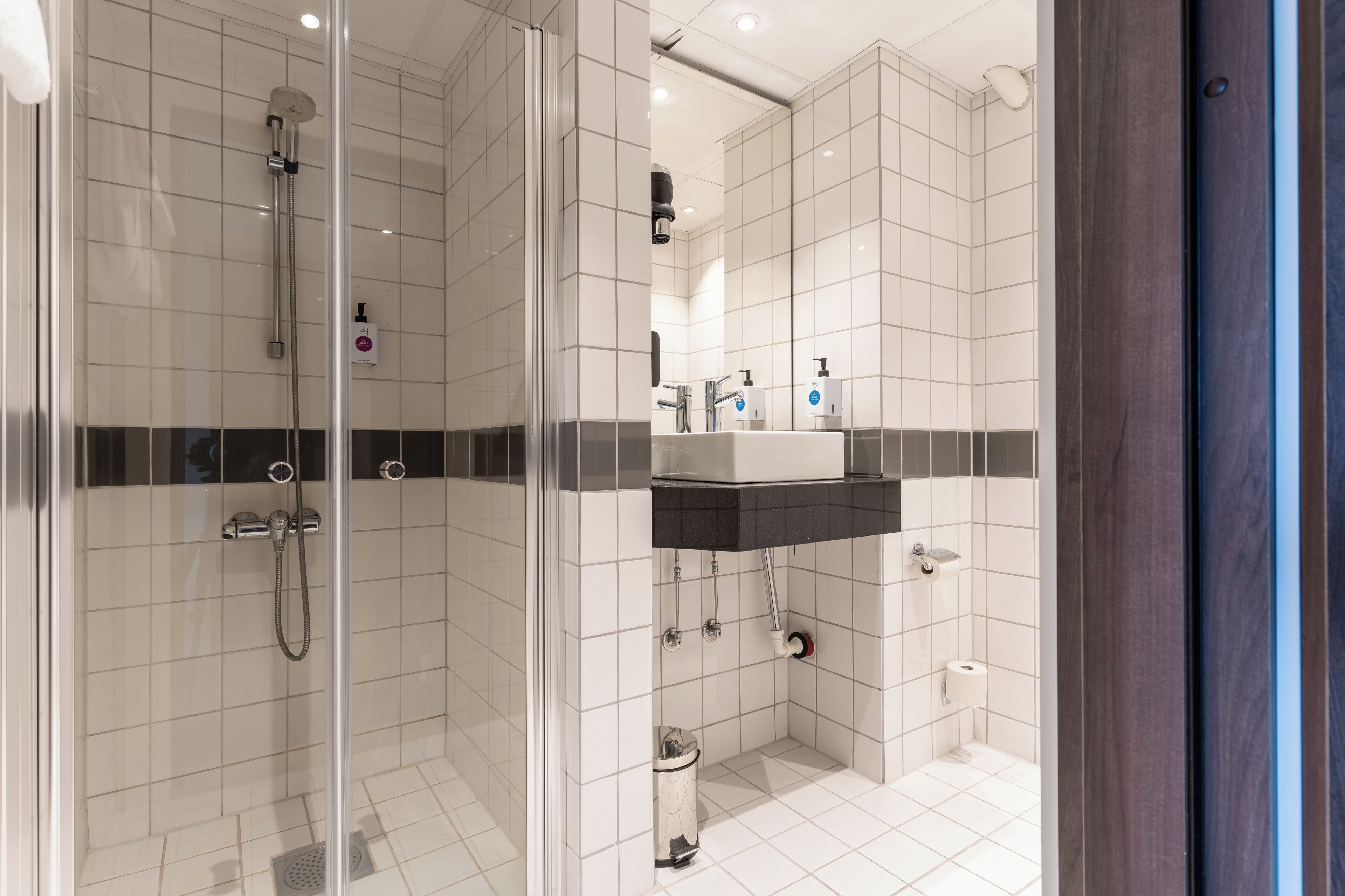 Ein modernes Badezimmer mit einer gläsernen Dusche, einem Waschbecken mit schwarzer Arbeitsplatte und einer Toilette.
