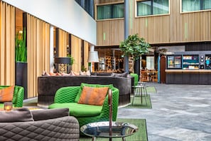 Un moderno vestíbulo de hotel con un sofá verde, un sillón negro y una pequeña mesa con una lámpara.