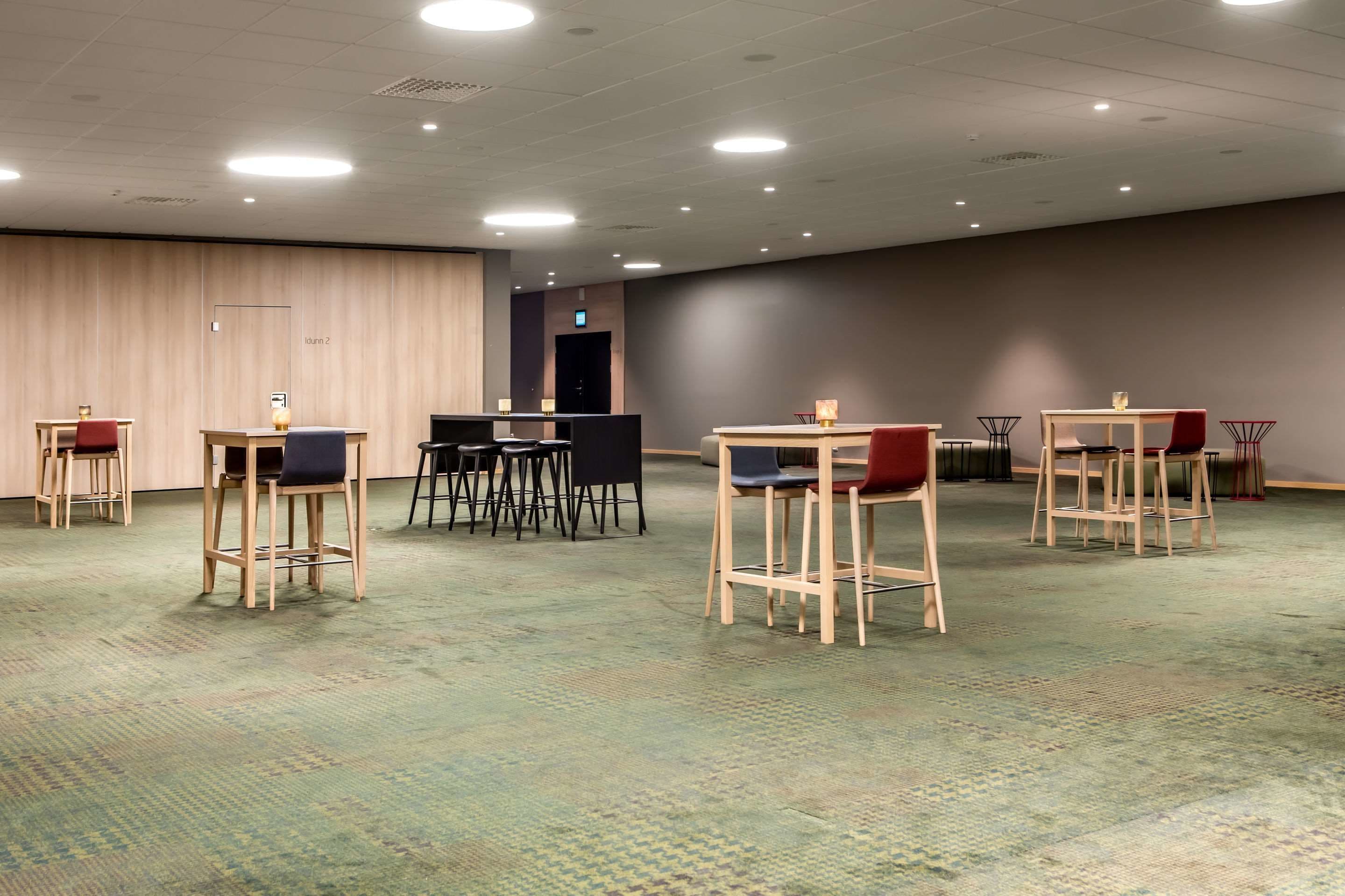 Een vergaderzaal met meerdere tafels en stoelen, een receptiebalie en een deur met de tekst 'Room 2'.