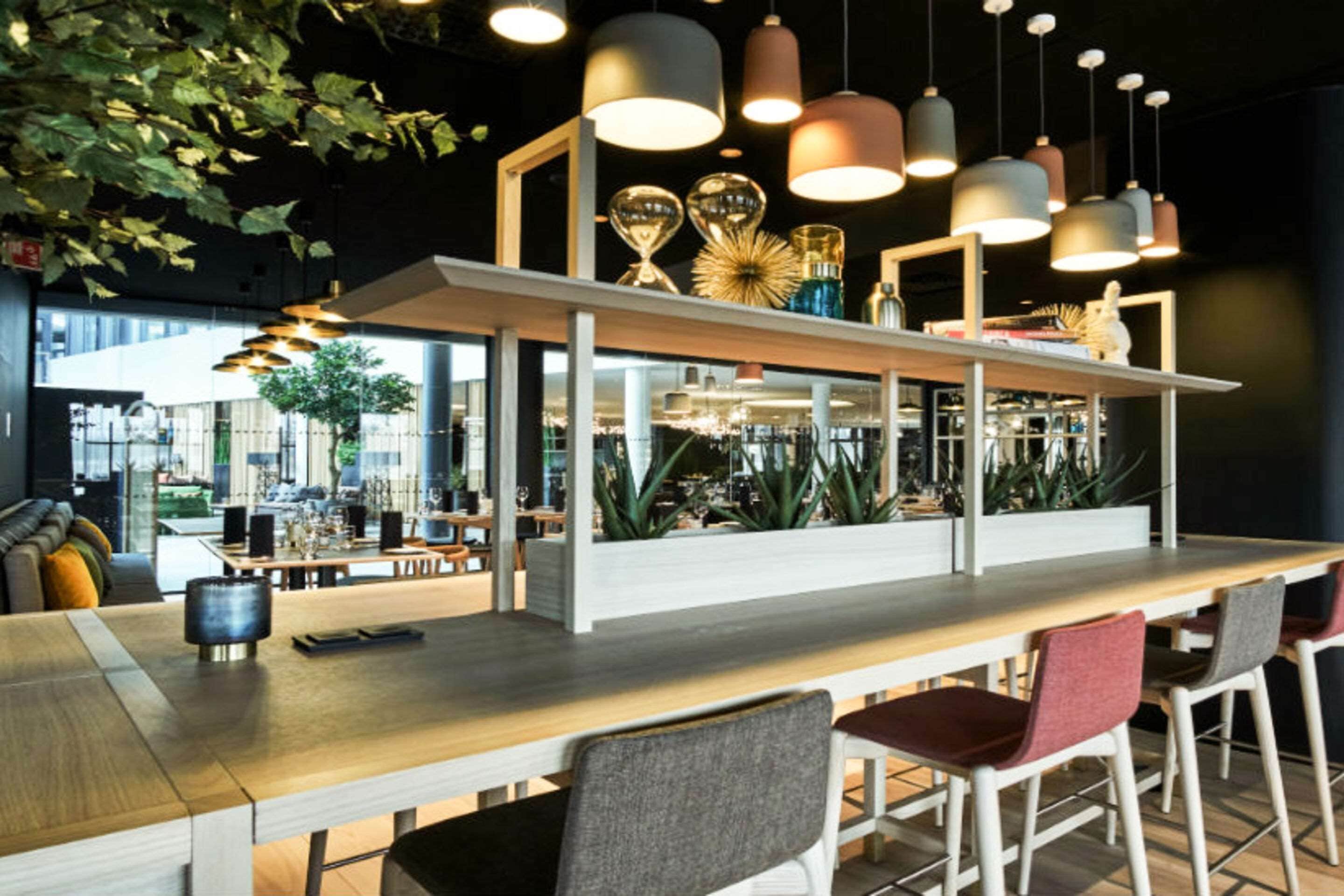 A modern bar area with a long wooden counter, multiple hanging pendant lights, and a variety of decorative items.