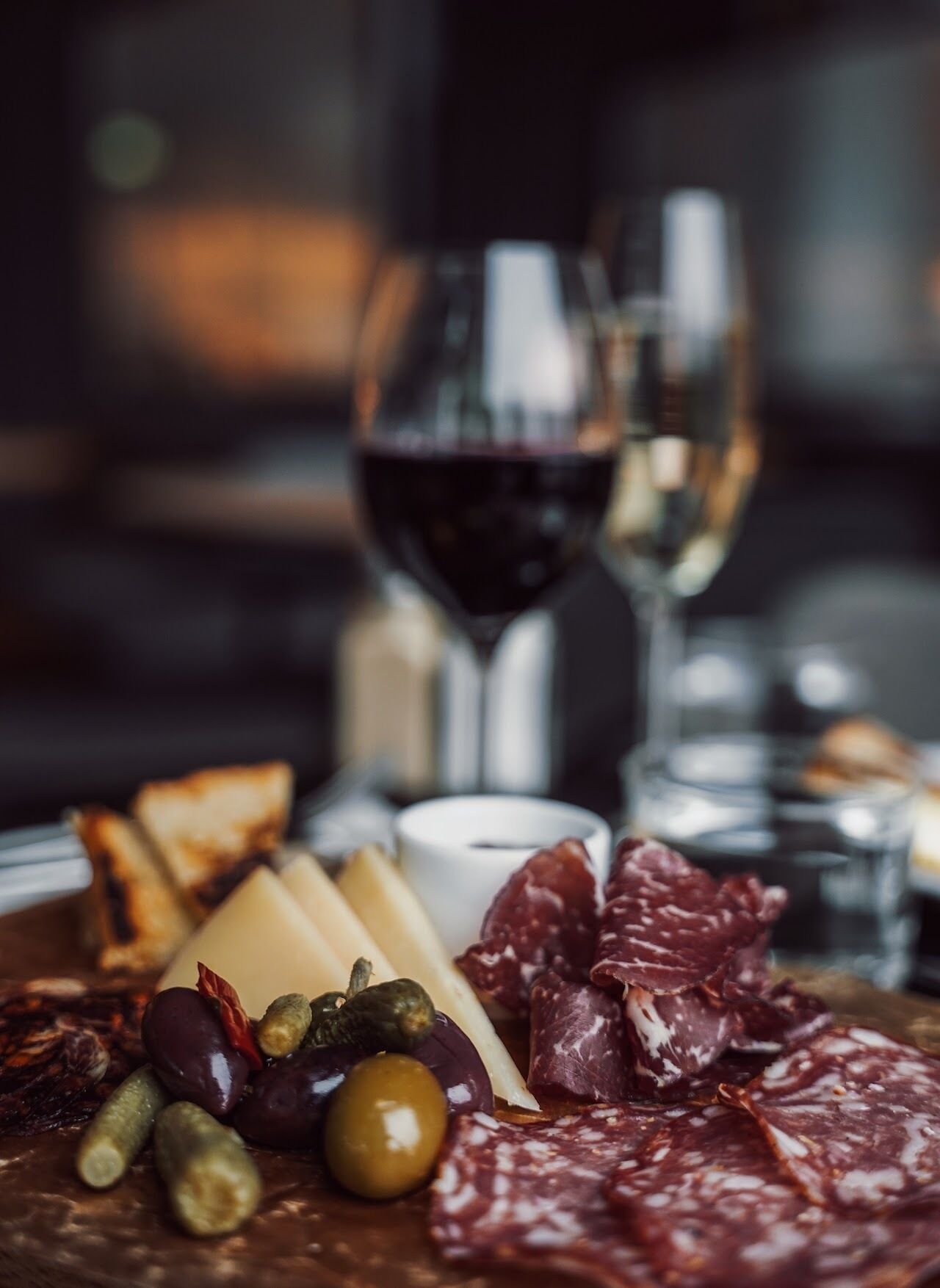 Un tagliere con salumi, formaggi e olive, accompagnato da calici di vino rosso.