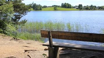 Un banco de madera junto a un lago, con un área verde y árboles al fondo.