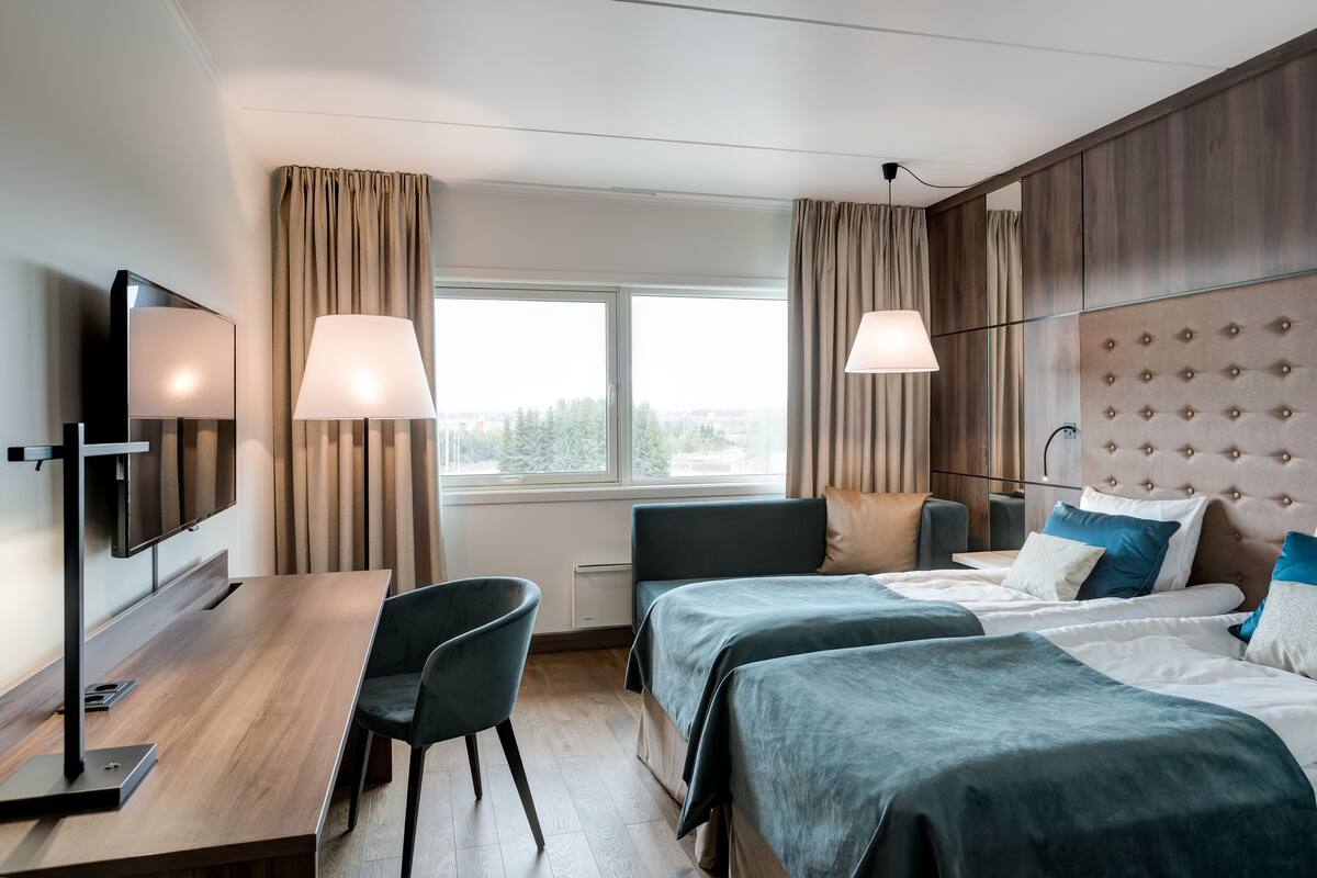 Een hotelkamer met twee bedden, een bureau, een stoel, een televisie en een raam met gordijnen.