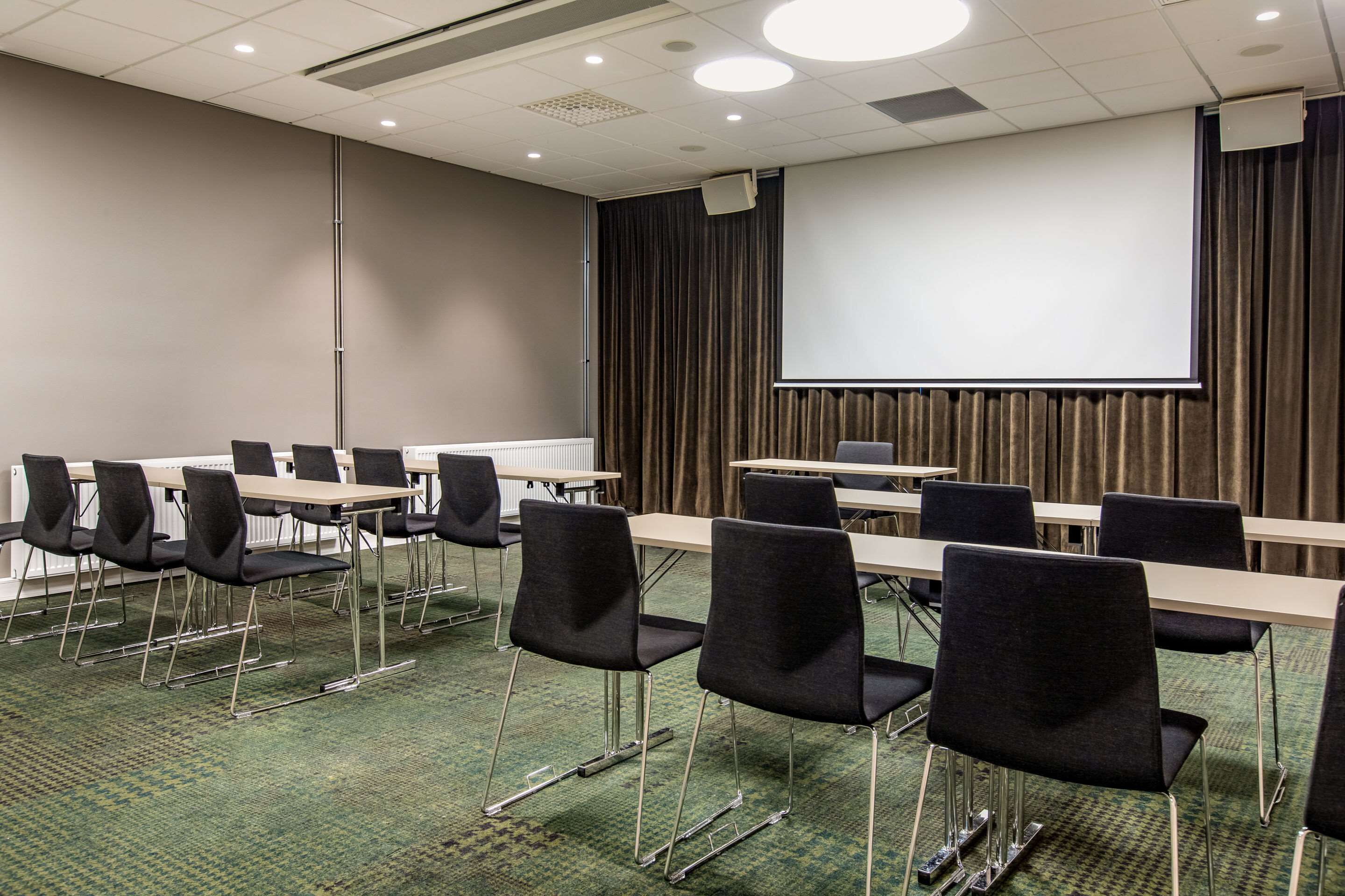 A conference room with a large screen, multiple tables, and chairs.