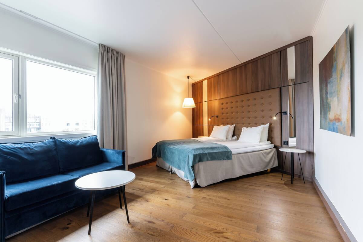 Een moderne hotelkamer met een bed, een bank, een eettafeltje en een groot raam.