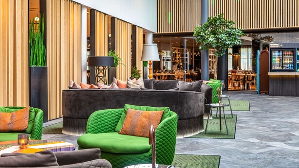 Eine moderne Hotelhalle mit einer grünen Sofagarnitur, einem Essbereich und einer Bar.
