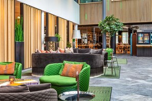 Eine moderne Hotelhalle mit einer grünen Sofagarnitur, einem Essbereich und einer Bar.