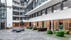 Eine großzügige Lobby mit mehreren Sitzbereichen, darunter grüne und graue Polstersofas sowie ein zentraler Couchtisch.
