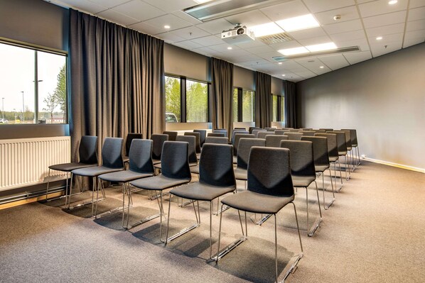 A conference room with rows of chairs, large windows, and a projector on the ceiling.