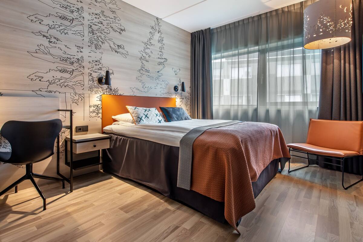 Een moderne hotelkamer met een groot bed, een bureau, een stoel en een groot raam met gordijnen.