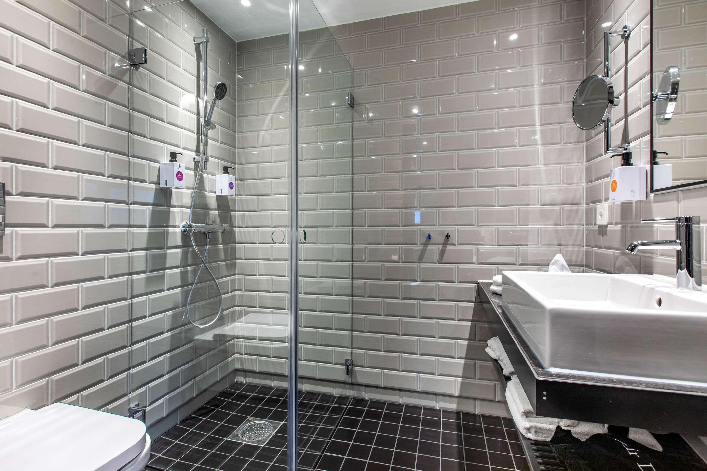 A modern bathroom with a glass-enclosed shower, a white sink, and a tiled floor.