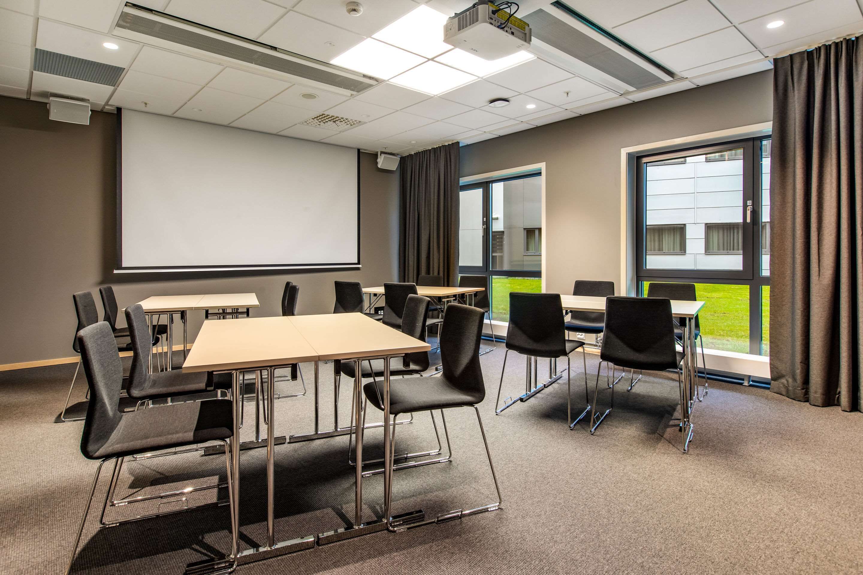 A conference room with a large screen, multiple tables, and chairs.