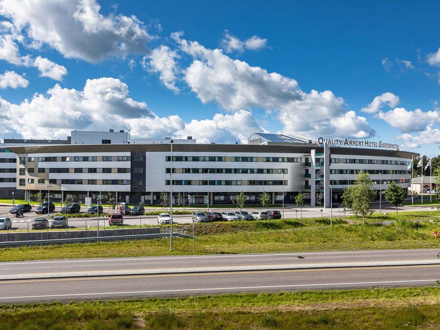 Un edificio moderno con tetto piatto, numerose finestre e un cartello con la scritta 'Quality Airport Hotel Gardermoos'.