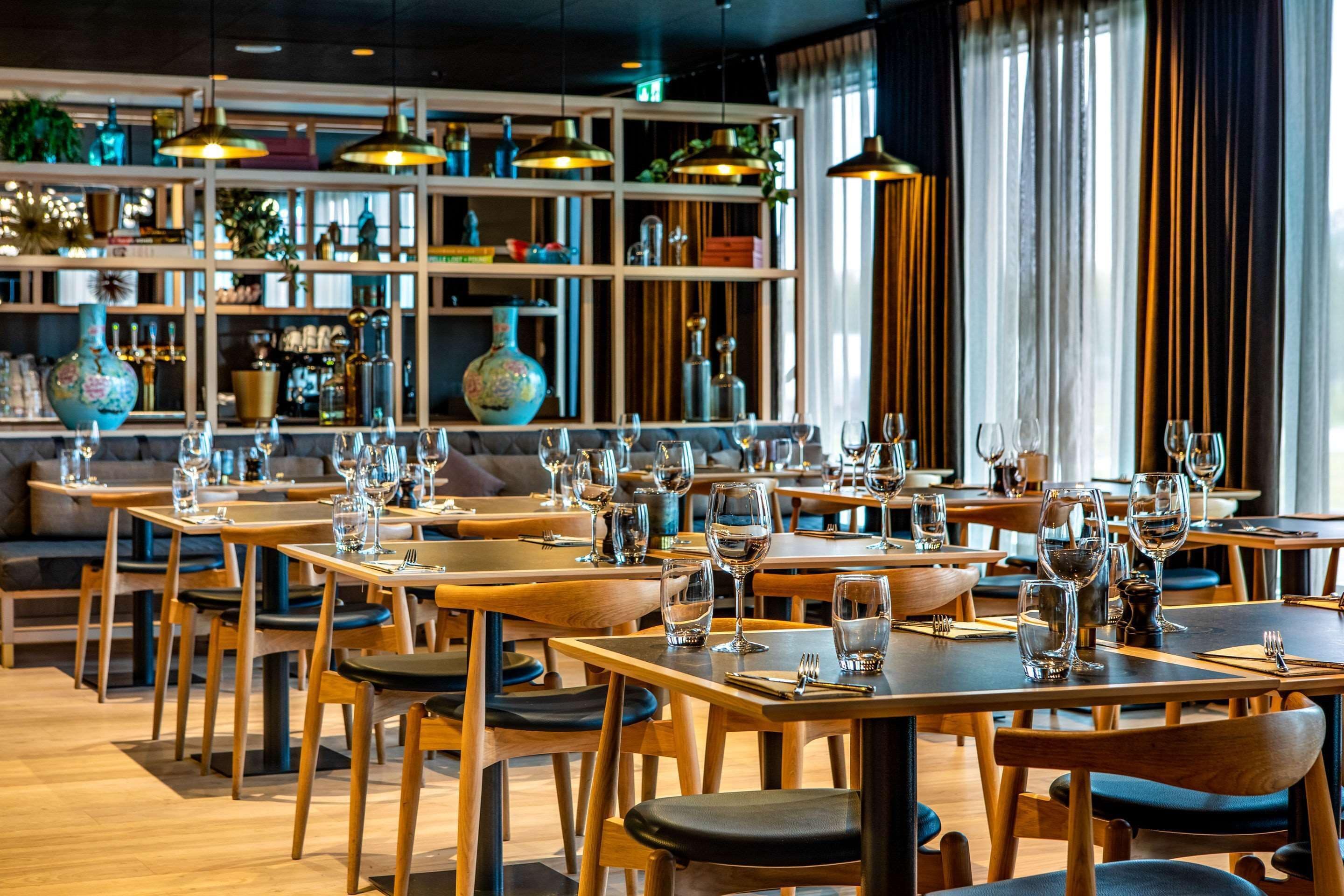 En restaurant med træborde og stole, reoler med pynteting og hængende pendellamper.