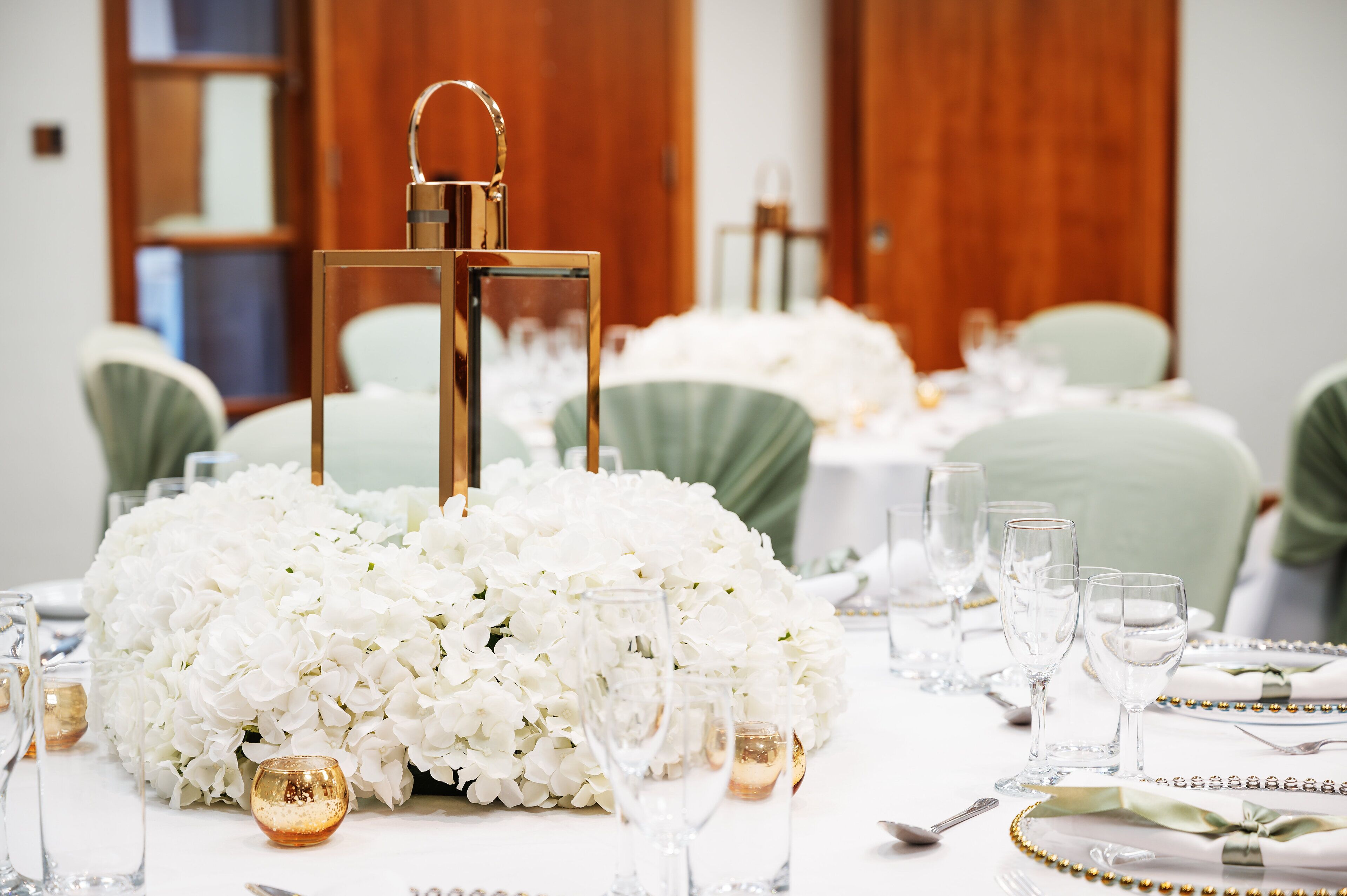 Une table décorée de fleurs blanches, de bougeoirs dorés et de verres transparents.