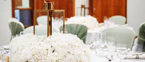 Une table décorée de fleurs blanches, de bougeoirs dorés et de verres transparents.
