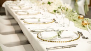 A table set with white plates, gold bead trim, and clear glassware.