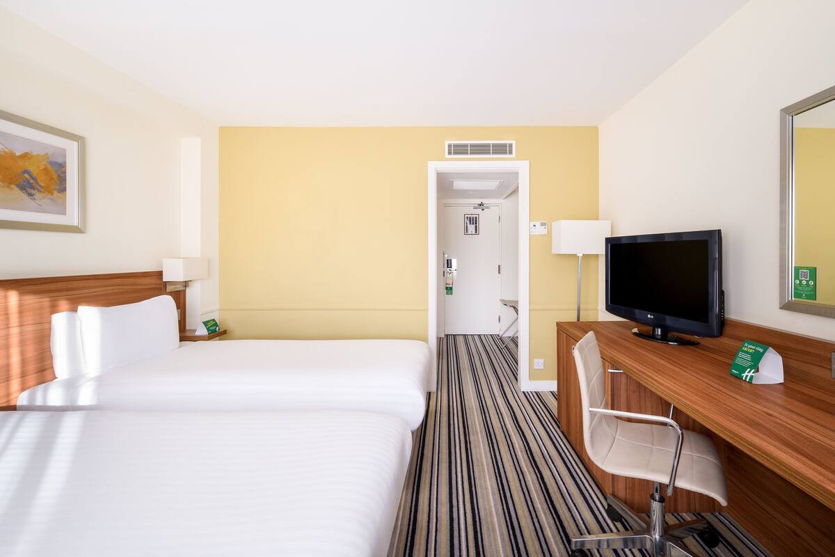 A hotel room with two beds, a desk with a television, a chair, and a door leading to a bathroom.