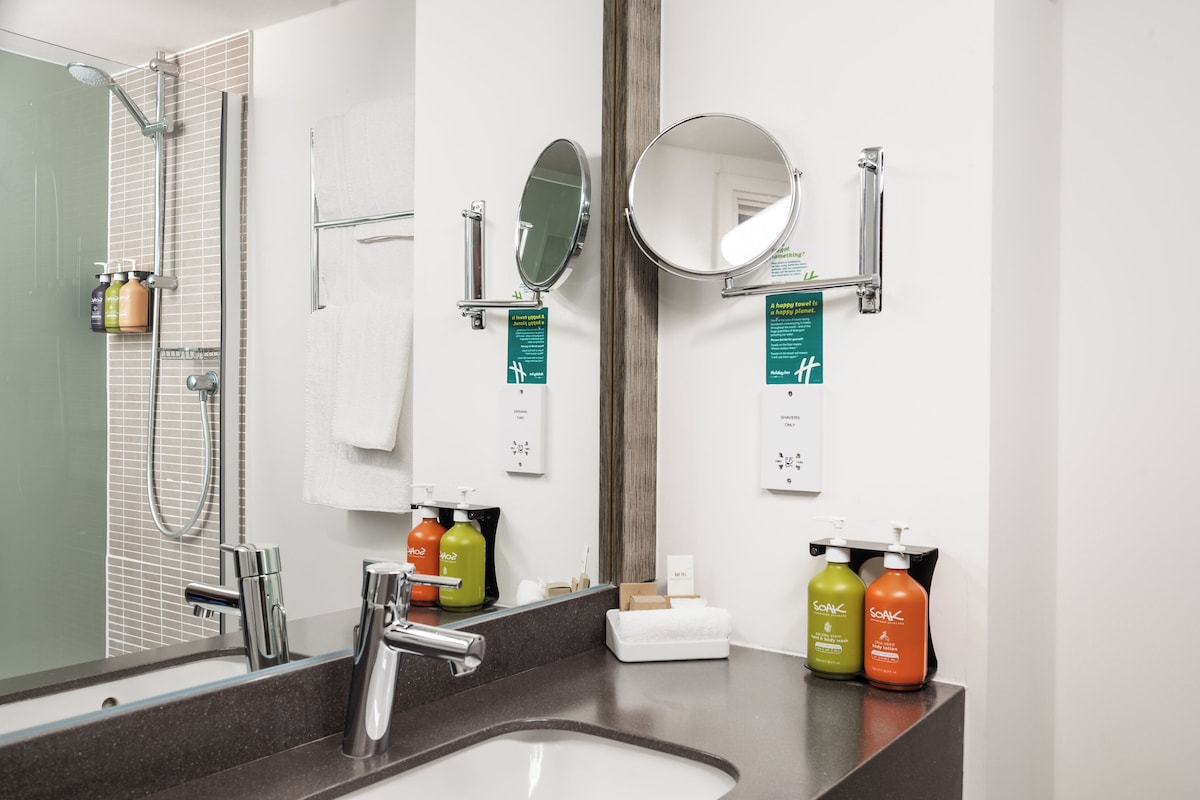 A bathroom with a sink, two mirrors, a towel rack, and toiletries.