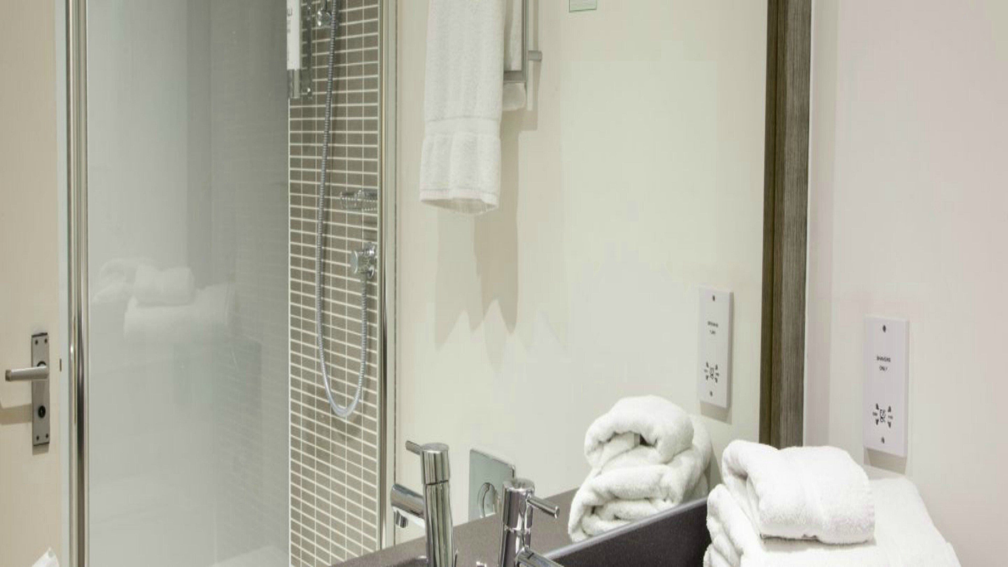 Un baño con cabina de ducha de vidrio, lavabo con espejo y toallero con toallas dobladas.