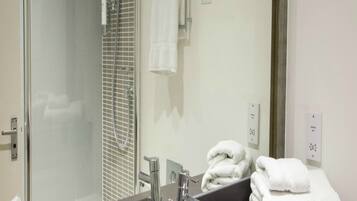 Un baño con cabina de ducha de vidrio, lavabo con espejo y toallero con toallas dobladas.