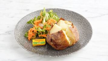 A plate with a baked potato, salad, and a small container of Anchor Butter.