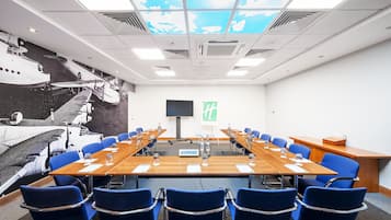 A conference room with a long table, blue chairs, a projector screen, and a mural of airplanes on the wall.