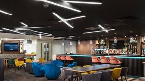 A modern bar area with a bar counter, colorful chairs, and a television mounted on the wall.