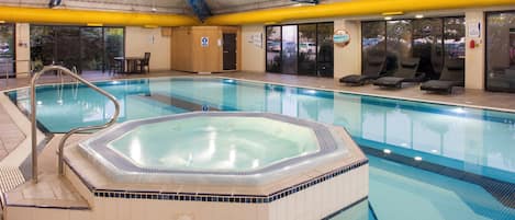 An indoor swimming pool with a hot tub, lounge chairs, and a covered roof structure.